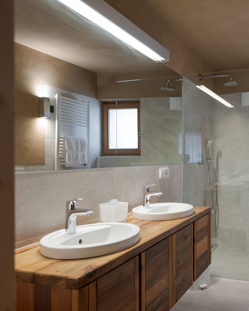 Badezimmer mit zwei Waschbecken, Spiegel, Dusche und Handtuchheizkörper